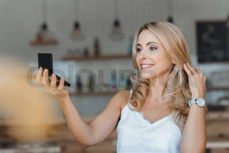 Beautiful smiling middle aged woman looking at cosmetic mirror, stock photo