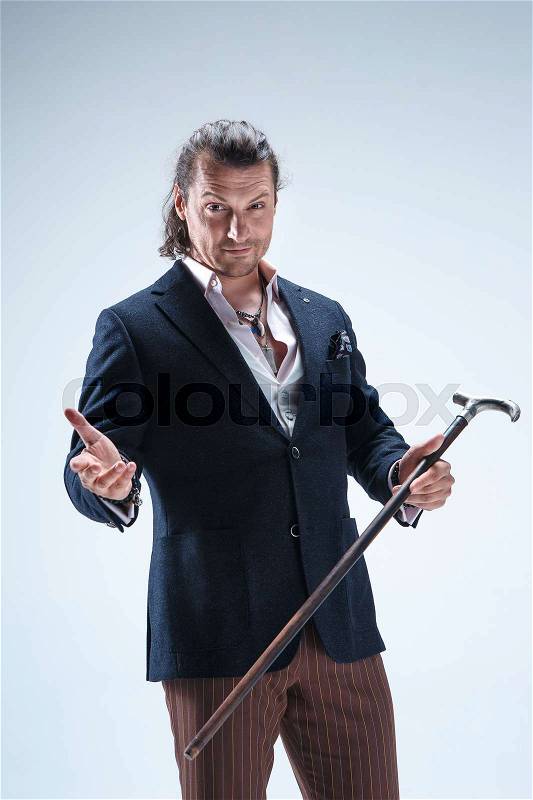 The mature bearded man in a suit holding cane. Isolated on a blue studio background, stock photo