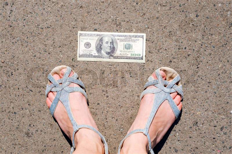 Lucky woman finding money on the street. Women feet next to hundred dollar bill. Lost and found money lying down on asphalt road, stock photo