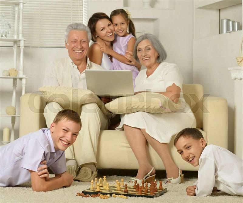 Portrait of big happy family, mother and daughter hugging, grandparents using laptop, sons playing chess, stock photo