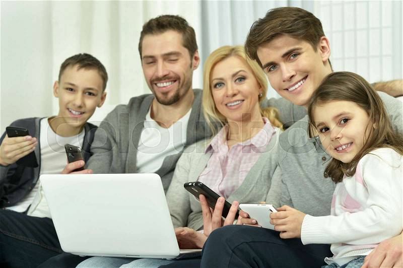 Family sitting on couch with laptop and other devices, stock photo