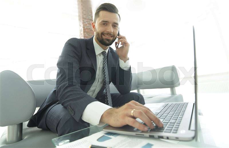 Busy businessman talks to a colleague through a modern phone and typing text on a laptop keyboard, stock photo