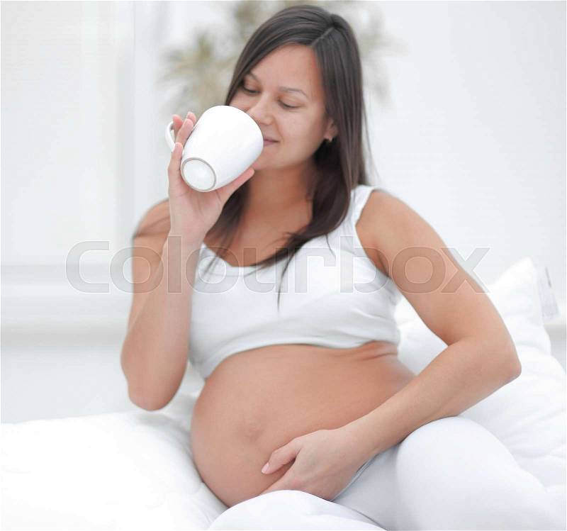 Happy pregnant woman drinking milk sitting in the living room. the concept of the care, stock photo