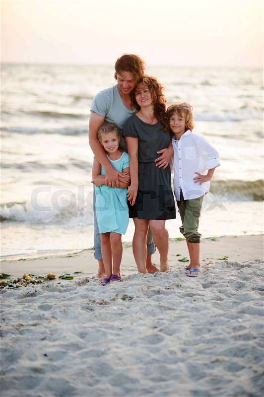 United family of four against the background of sea waves. Mom, dad, and two children standing arm in arm on a sandy beach, stock photo
