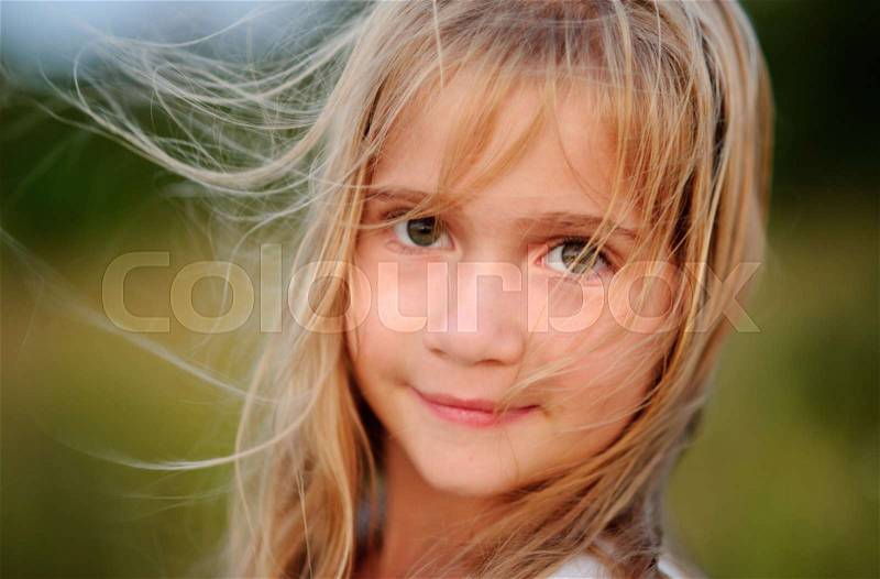 Portrait of the charming girl of 9-10 years. Wind plays with long blonde hair. Serious look of big green eyes. Gentle half-smile, stock photo