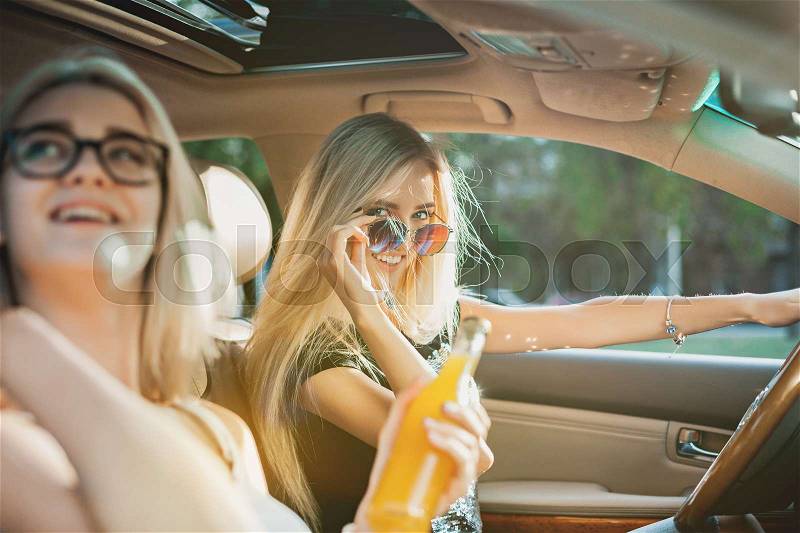 The young women in the car sitting and smiling outdoor with bottle of juice. The lifestyle, travel, adventure and female friendship concept, stock photo