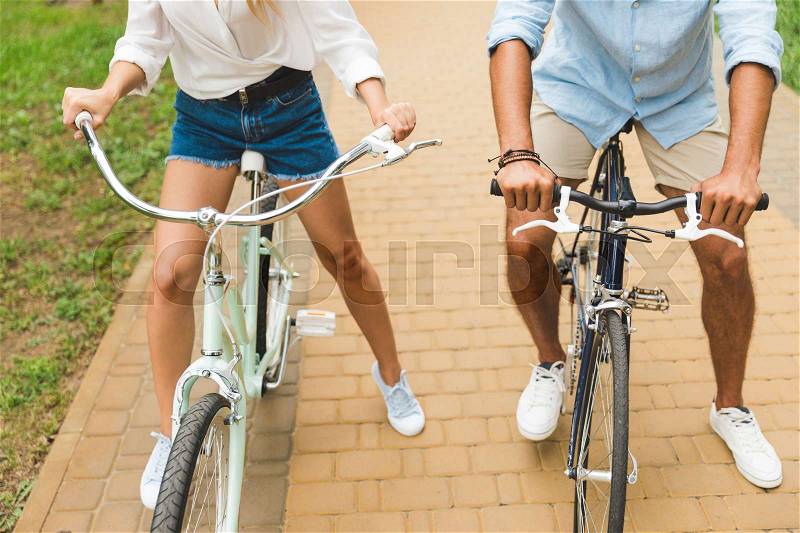 Cropped shot of couple holding hands on bicycle handle bars in park, stock photo