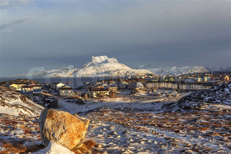 Daylight view to the distant houses of suburb of Nuuk city, with stones, snow and Sermitsiaq mountain in the background, Greenland, stock photo