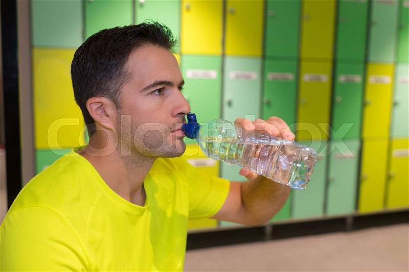 Sports man drinking water in the locker room, stock photo