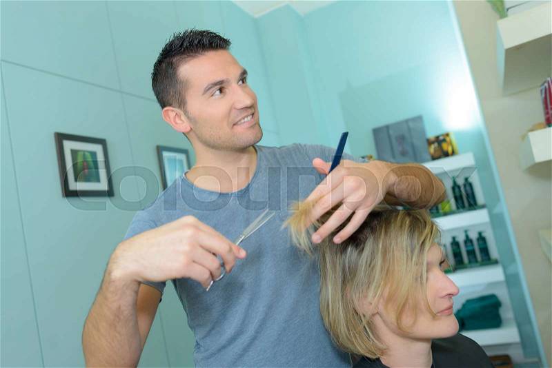 Male hairdresser is making a haircut for a woman, stock photo
