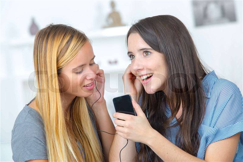 Two beautiful girls sharing headphones listening to music, stock photo