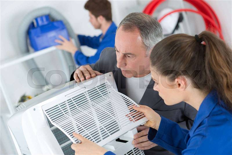 Female apprentice learning to repair industrial air conditioning compressor, stock photo