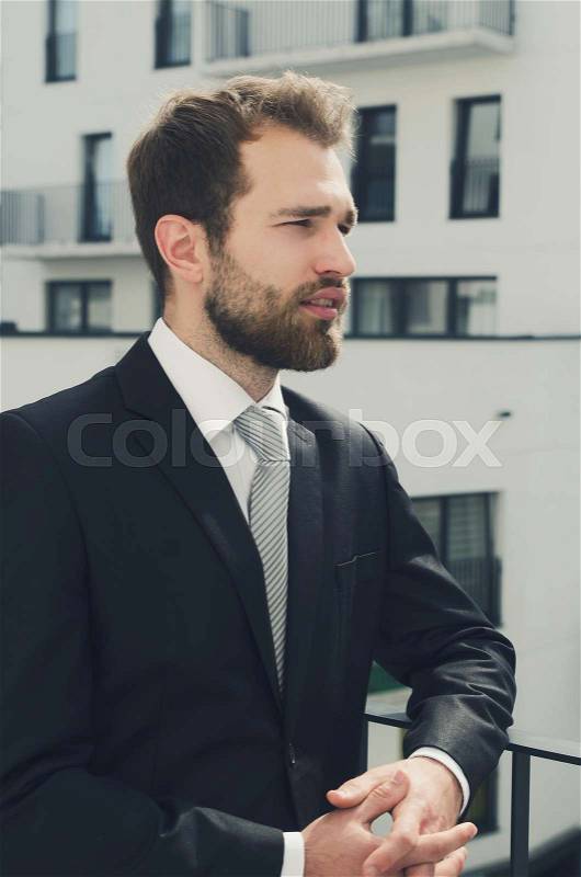 Relaxed businessman standing on balcony of his apartment. businessman outdoor friendly caucasian suit balcony city apartment concept, stock photo