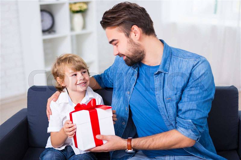 Birthday or christmas concept - young father giving gift to his happy son, stock photo
