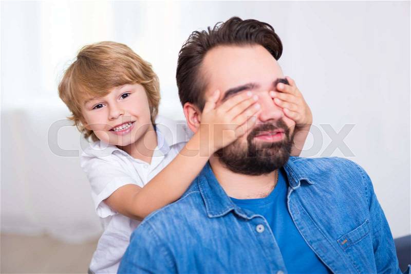Surprise concept - little son covering eyes of his father at home, stock photo