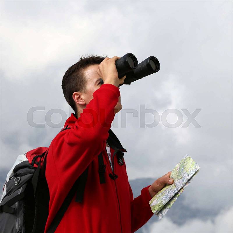 Young man is searching the destination with binoculars in the mountains, stock photo