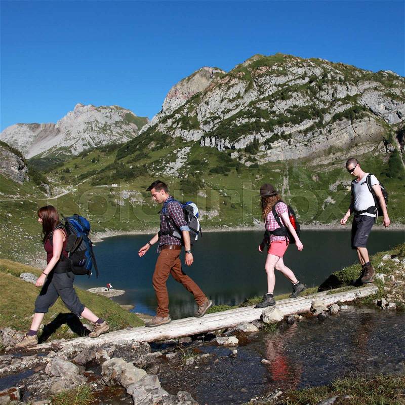 Young people cross a brook in the mountains during a hiking tour, stock photo