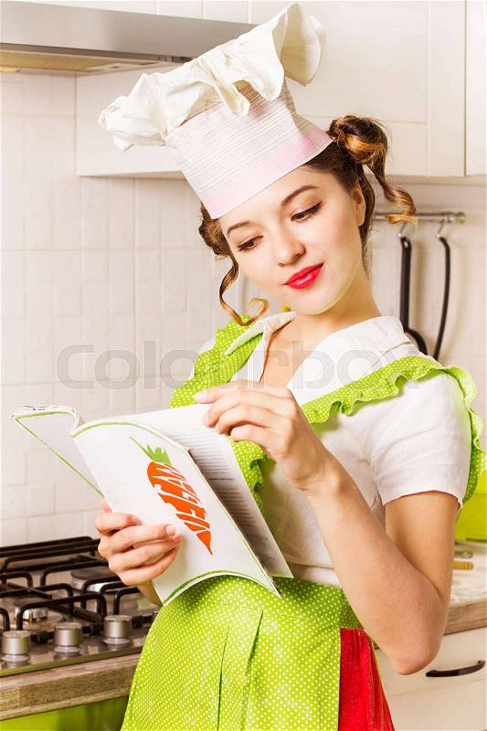 Beautiful young chef reading a vegan cooking recipe book in the kitchen, stock photo