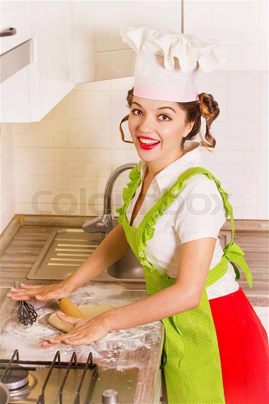 Smiling young woman chef in chef hat cooking dough with help rolling pin in kitchen, stock photo