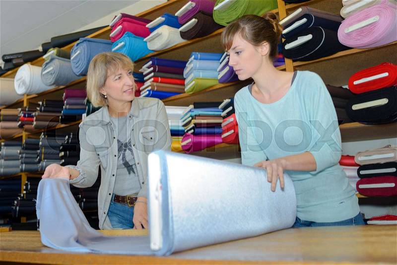 Beautiful brunette choosing fabric skeins in textile shop, stock photo