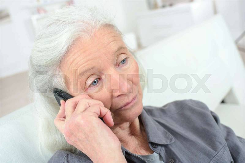 Sad old woman talking on the phone, stock photo
