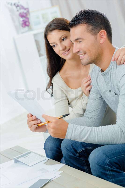 Young happy couple sitting on sofa calculating budget, stock photo