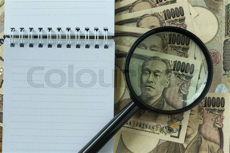 White notebook with copy space and magnifying glass on pile of japanese yen banknotes as financial concept, stock photo