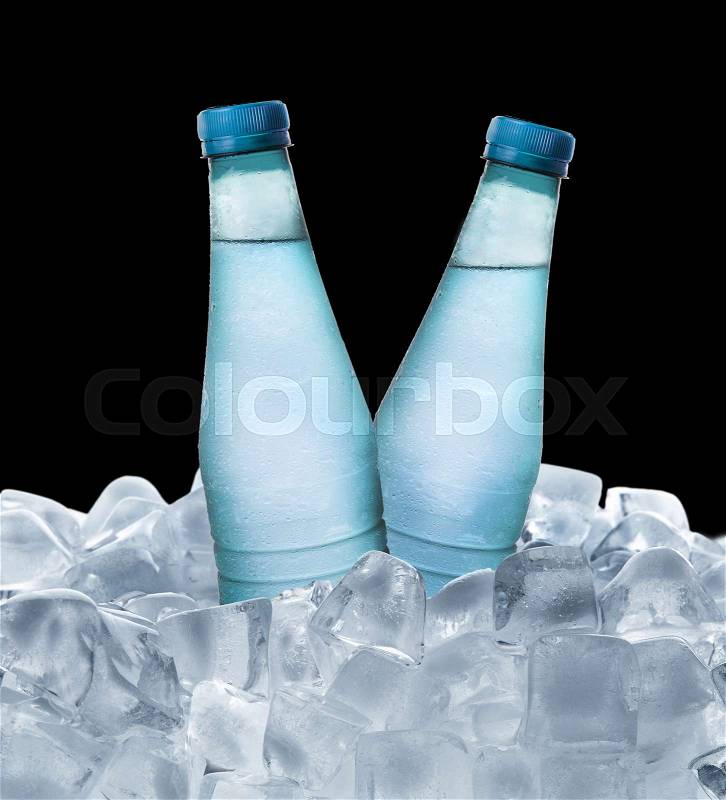 Cold water bottle in ice cube over dark background, stock photo
