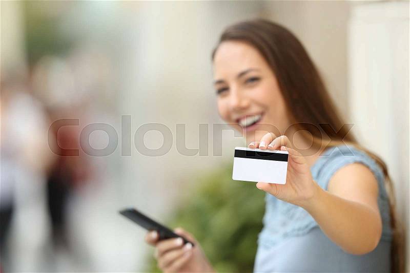 Happy on line buyer showing a credit card to the camera on the street, stock photo