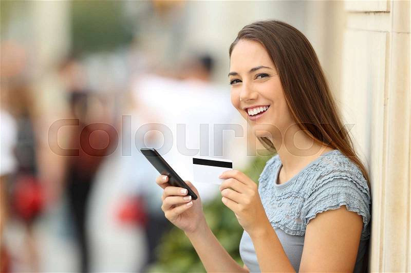 Portrait of an on line shopper looking at camera and holding a credit card on the street, stock photo