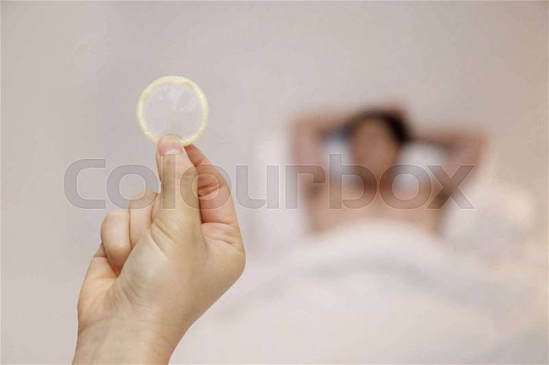 Woman holding condom with a man lying on bed, stock photo