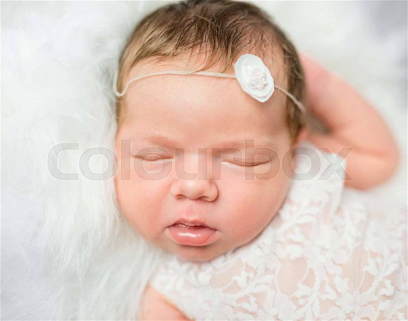 Cute face of sleepy newborn baby with hair band lying on soft blanket, stock photo