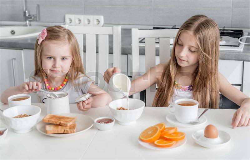 Two lovely sisters at the table eating healthy breakfast with toasts with honey and milk, stock photo