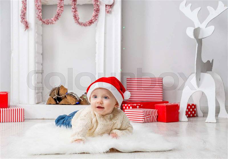 Funny little baby in red hat on the floor in decorated holiday roone, stock photo