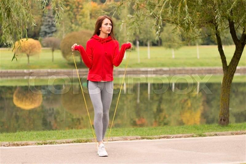 Outdoor shot of focused young woman with jump rope outdoors in nature. Fitness female exercising with jump rope in a park on a sunny day, stock photo