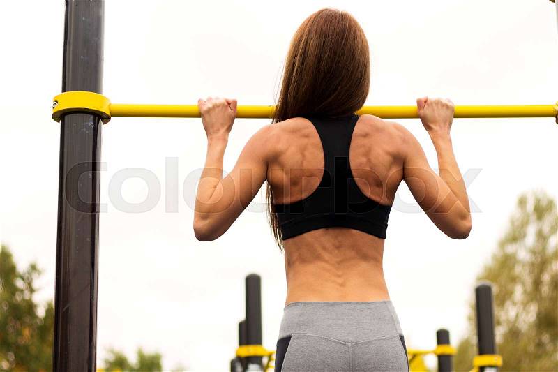 Rear view of woman doing chin-ups on the gym bar, stock photo
