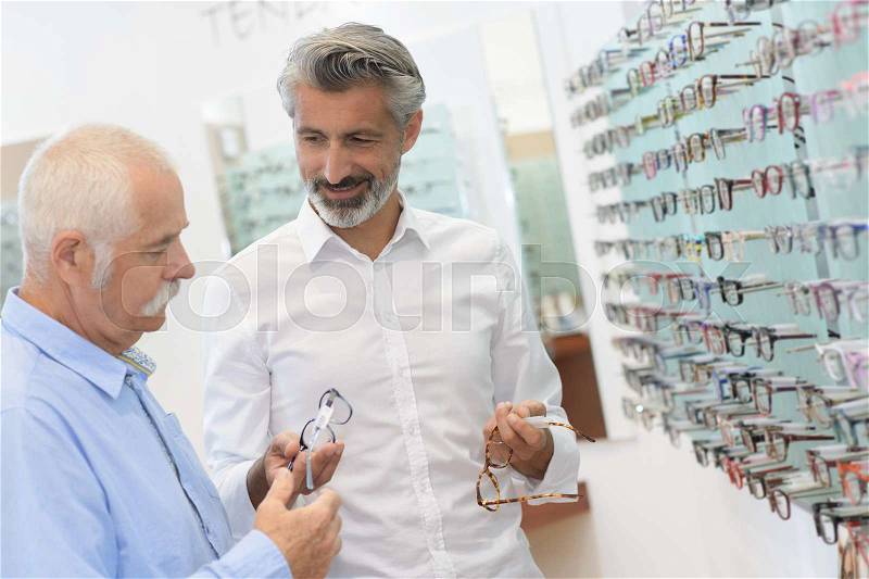 Optician and man choosing a new pair of glasses, stock photo