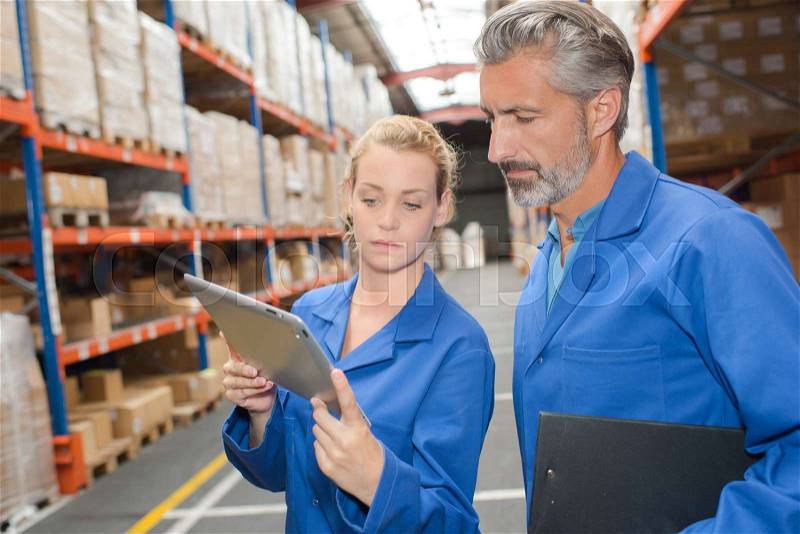 Warehouse manager writing on clipboard in warehouse, stock photo
