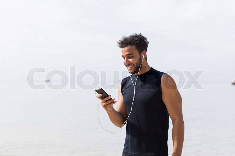 Hispanic Male Runner Using Cell Smart Phone On Beach While Jogging On Seaside Man Young Happy Smiling Latin Sport Healthy Lifestyle Concept, stock photo