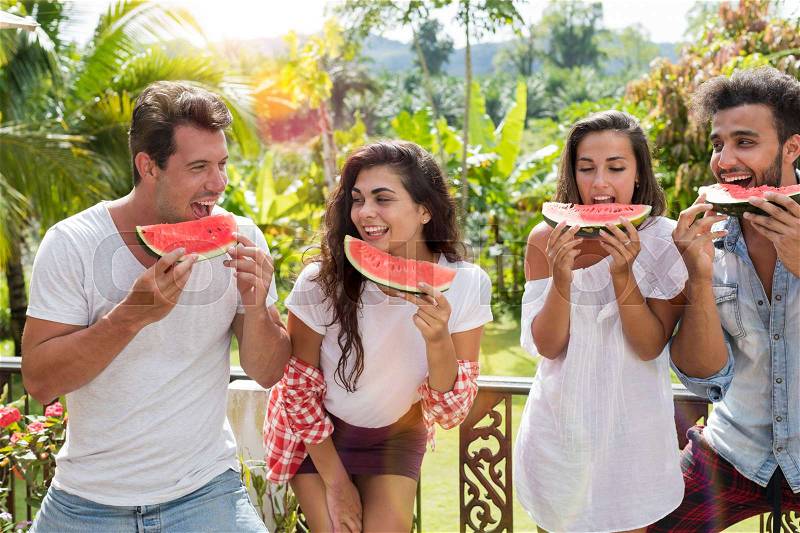 Cheerful Group Of Friends Eating Watermelon Together Outdoors On Summer Terrace With Tropical Forest Background Mix Race People Having Fun Frinedship And Summer Concept, stock photo