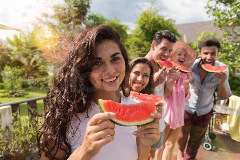 Cheerful Woman Holding Watermelon Slice Smile Together With Group Of Friends Eating Water Melon Together On Summer Terrace In Tropical Forest, stock photo