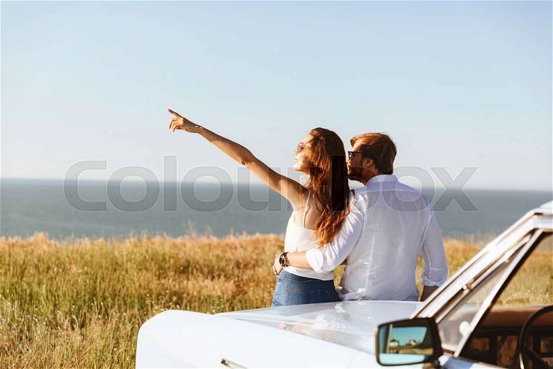 Back view of Young lovely couple standing near the retro car while woman, stock photo