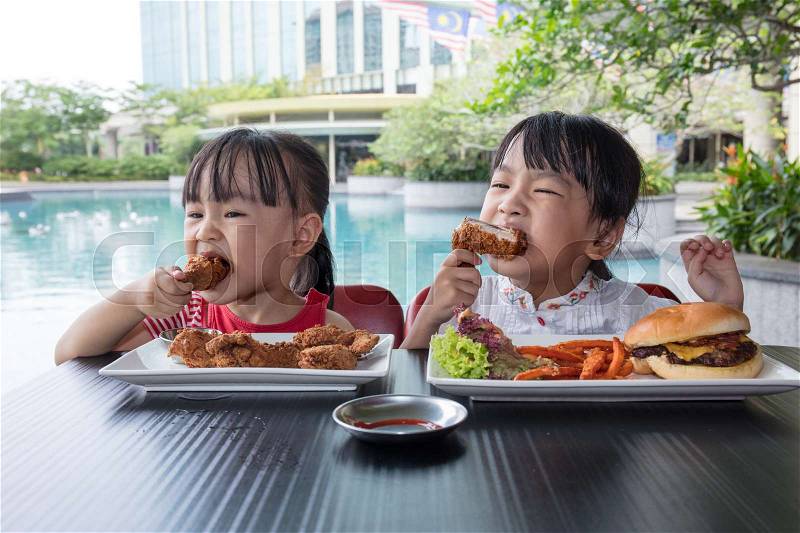 Asian Little Chinese Girls Eating Burger and Fried chicken at Outdoor Cafe, stock photo