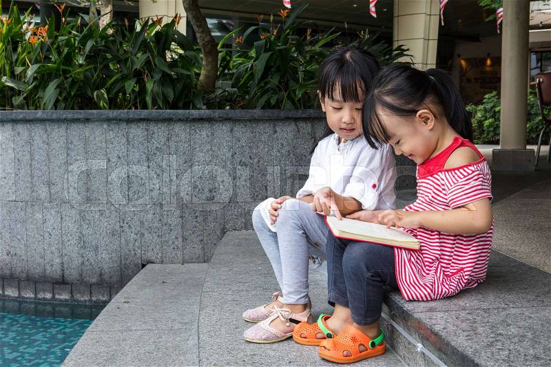Asian Little Chinese Girls reading a book beside the fountain outdoor, stock photo