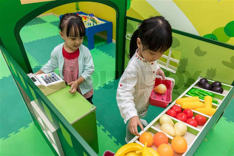 Asian Chinese little girls role-playing at fruits store at indoor playground, stock photo