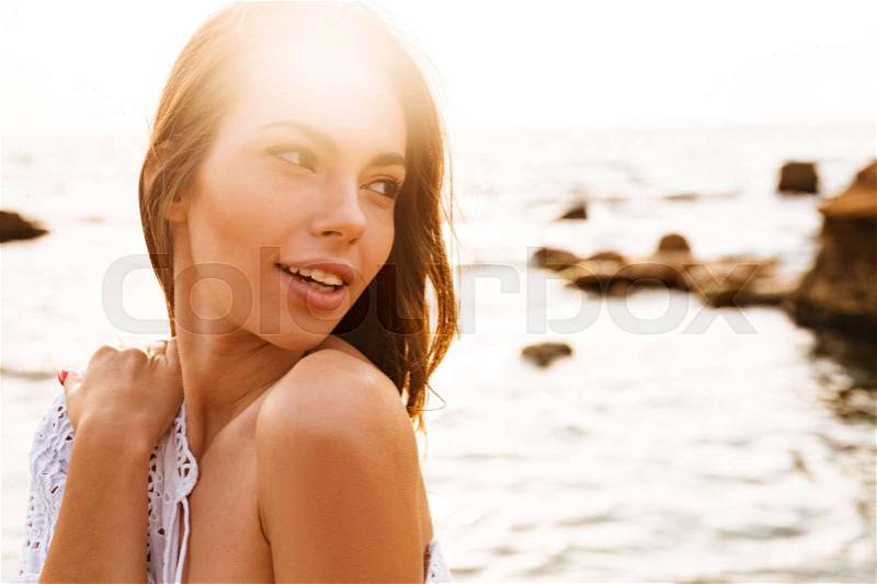 Close up picture of pretty woman posing sideways on beach and looking back, stock photo