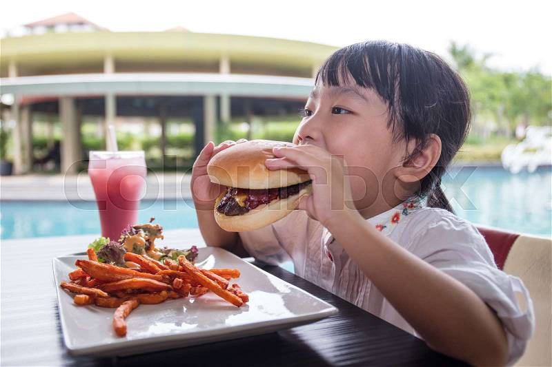 Asian Little Chinese Girl Eating Burger and French fries at Outdoor Cafe, stock photo