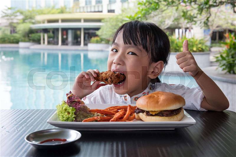 Asian Little Chinese Girl Eating Burger and Fried chicken at Outdoor Cafe, stock photo
