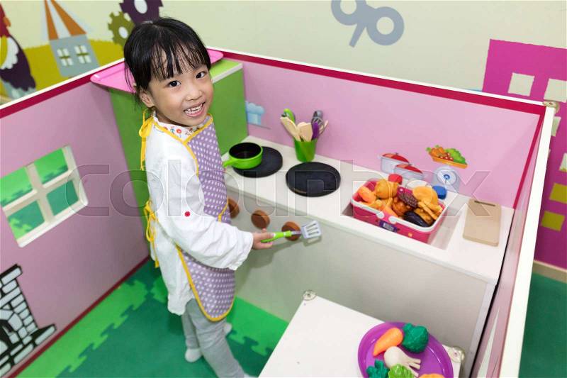 Asian Chinese little girl role-playing at kitchen at indoor playground, stock photo