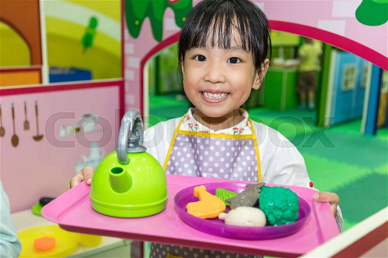 Asian Chinese little girl role-playing at kitchen at indoor playground, stock photo
